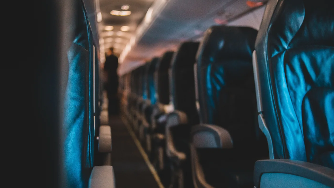 Fileiras de poltronas de avião vazias, mostrando o espaço entre os assentos