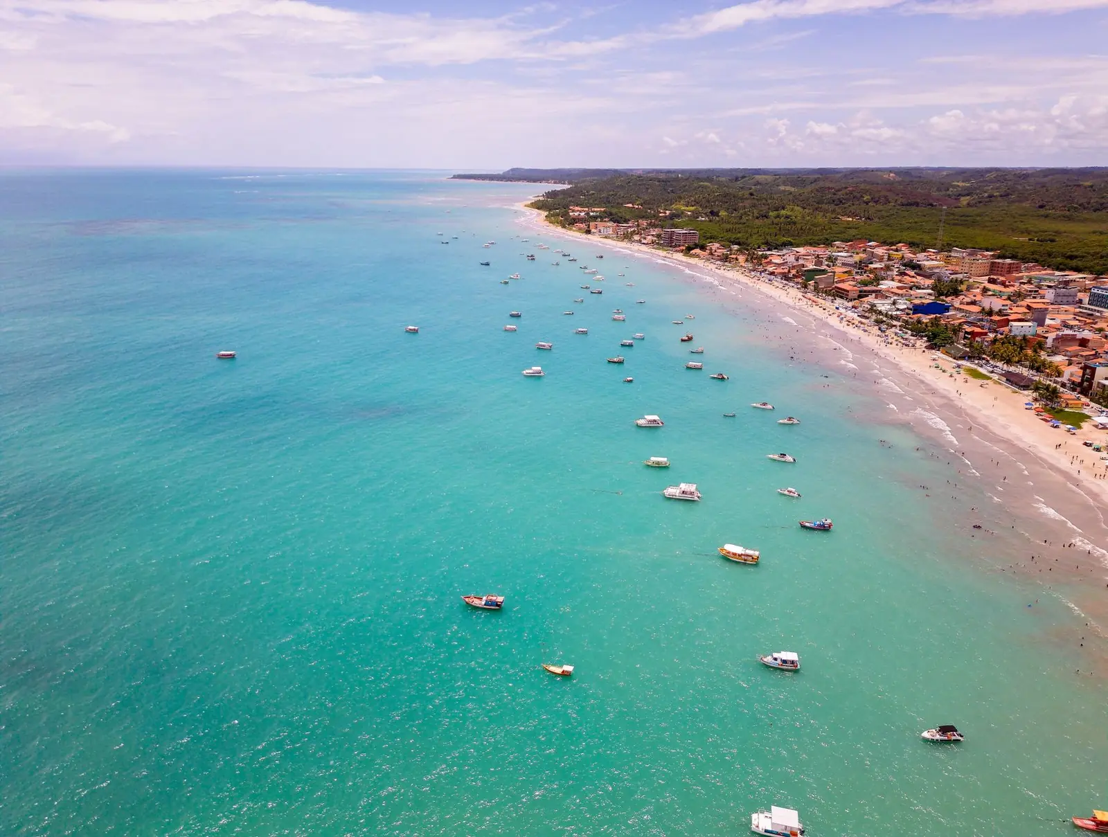 Vista aérea da praia de Maragogi com dezenas de barcos sobre o mar turquesa