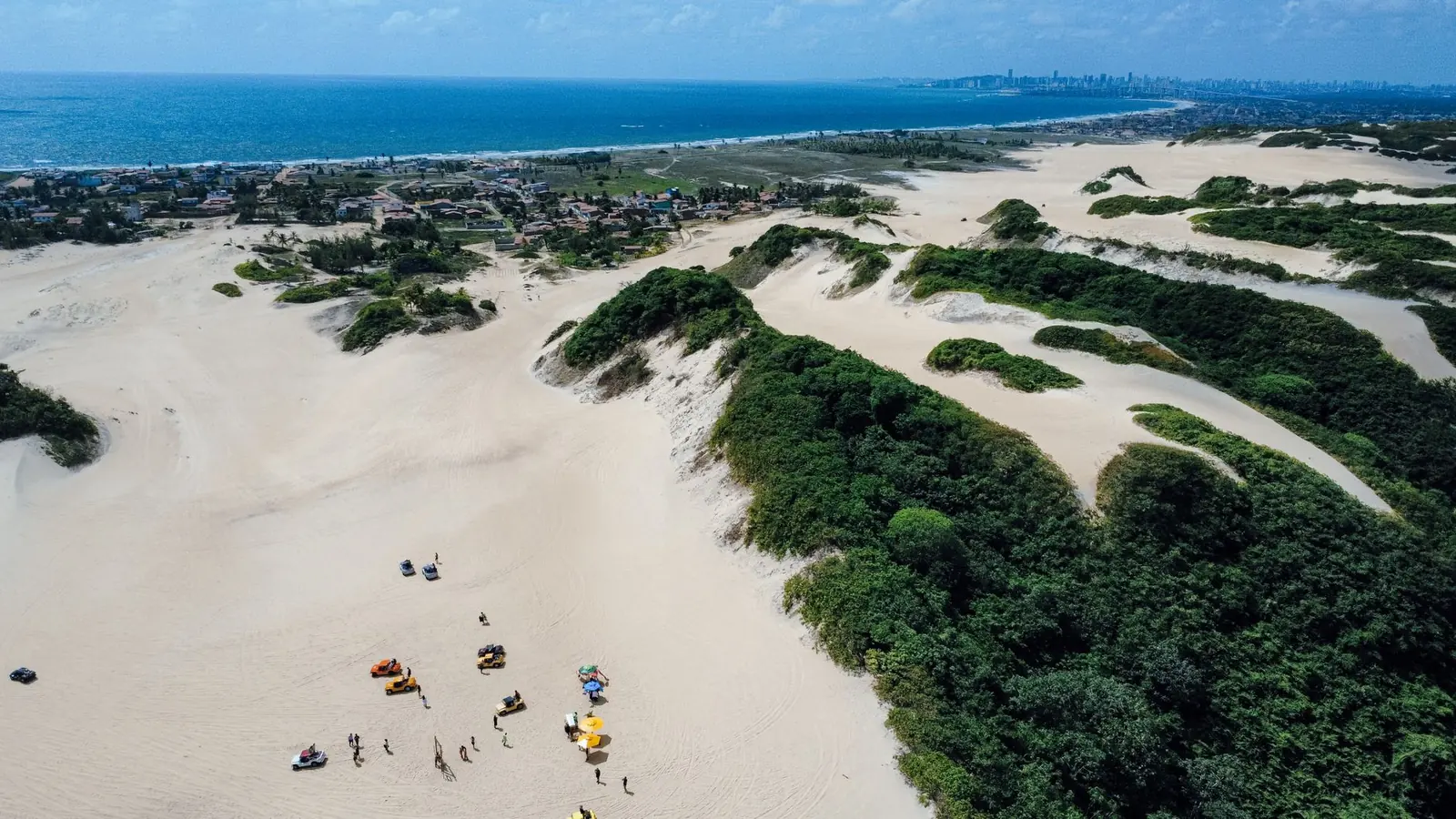Vista aérea das dunas brancas de Genipabu em Natal, com vegetação verde e o mar ao fundo