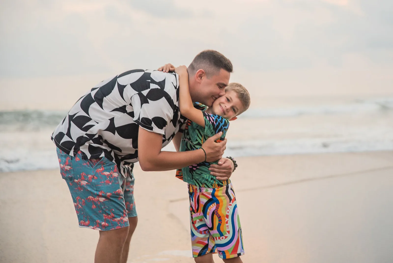 Pai e filho abraçados na areia de uma praia tropical durante as férias