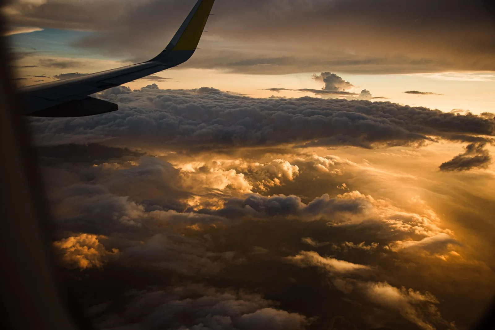 Asa de avião sobre nuvens douradas ao pôr do sol vista da janela