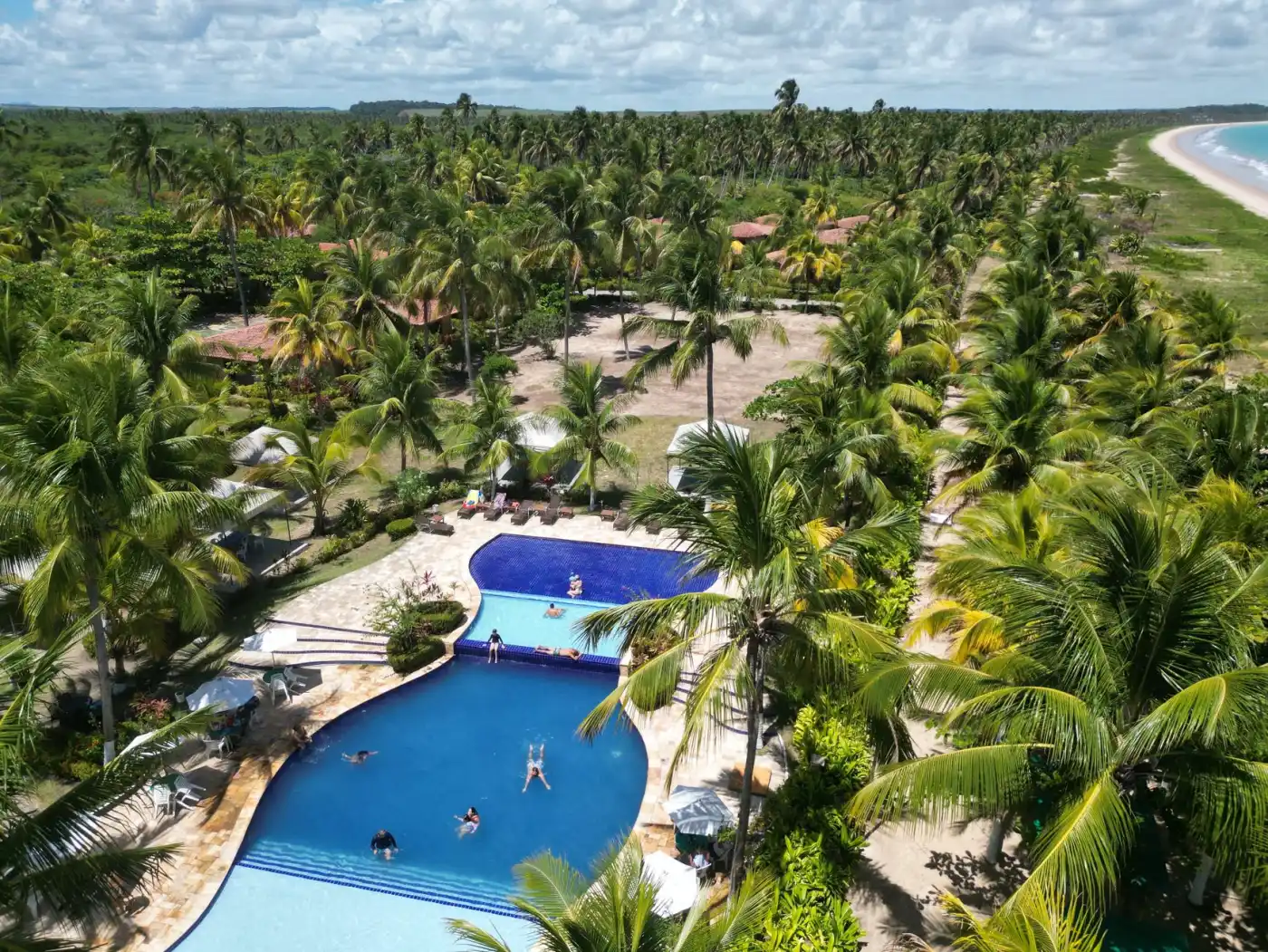 Vista aérea de resort à beira-mar com piscinas e coqueiros no Nordeste