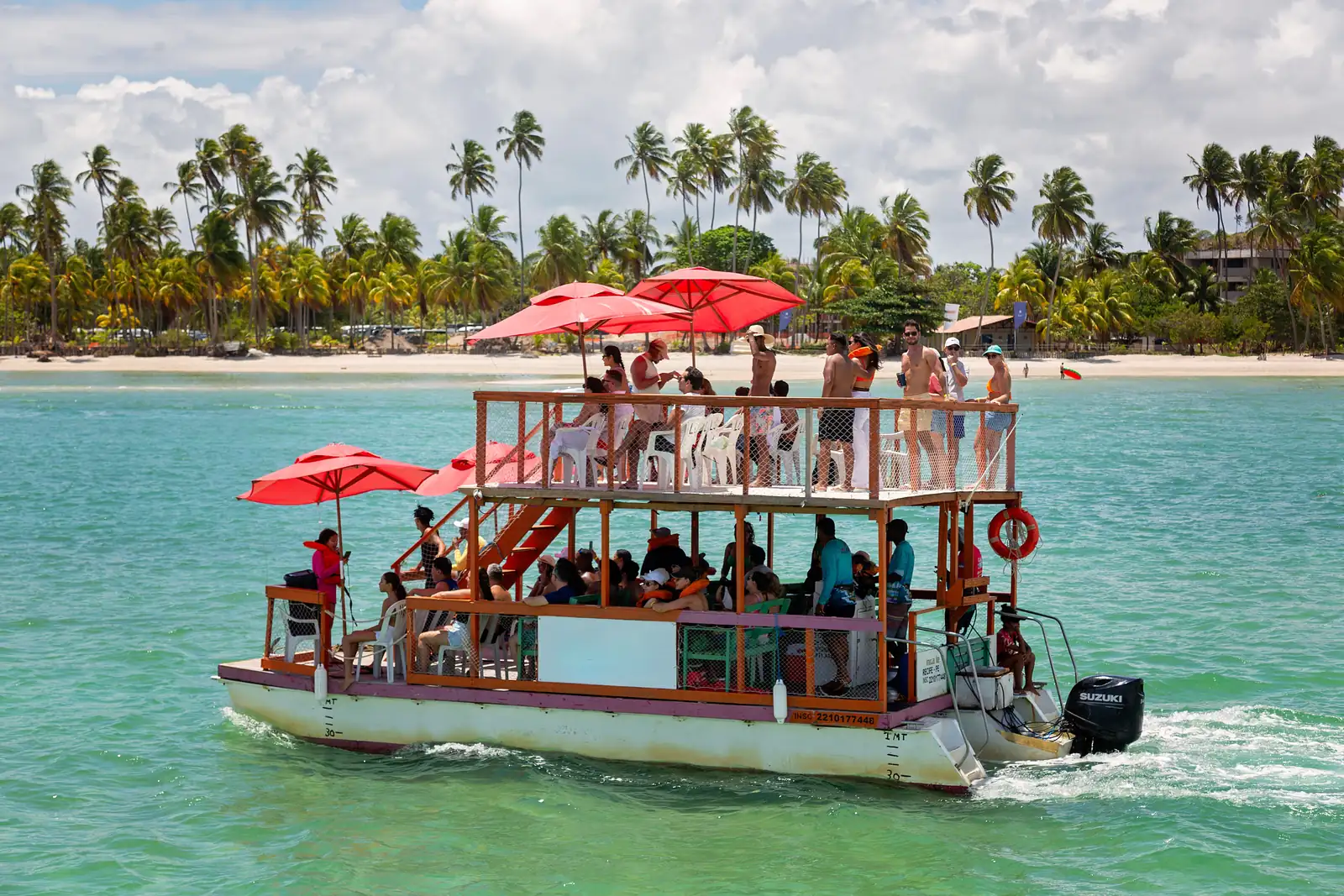 Turistas em passeio de barco com guarda-sóis vermelhos no mar verde do litoral de Pernambuco